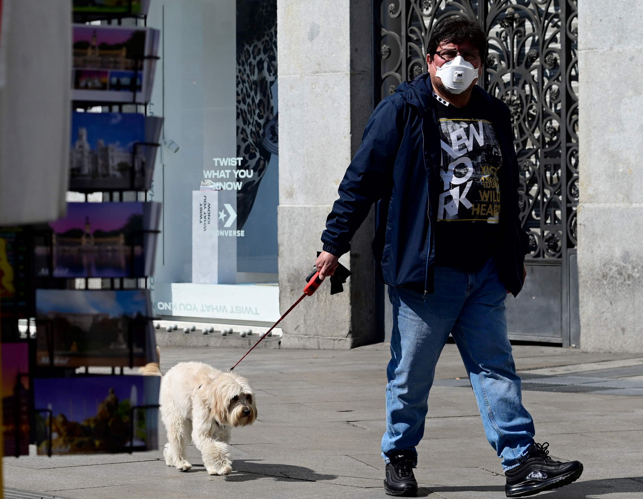 Hombre con mascarilla pasea a su perro en Madrid, España. Foto: AFP.
