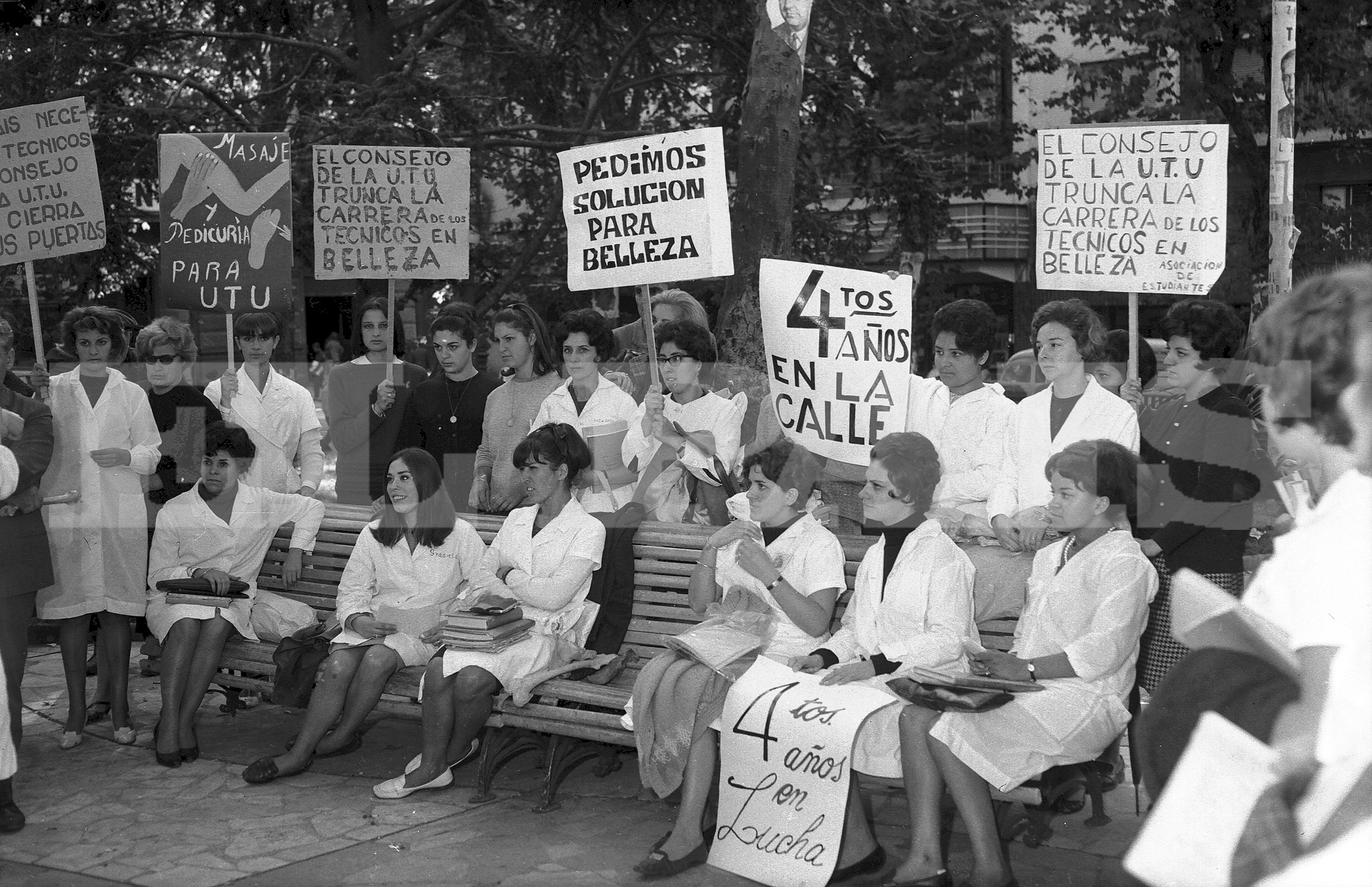 Manifestación con carteles y túnicas. Un grupo de estudiantes de la carrera de Belleza en la UTU difunden sus reclamos en una plaza, a comienzos de la década de 1960. Foto: Archivo El País.