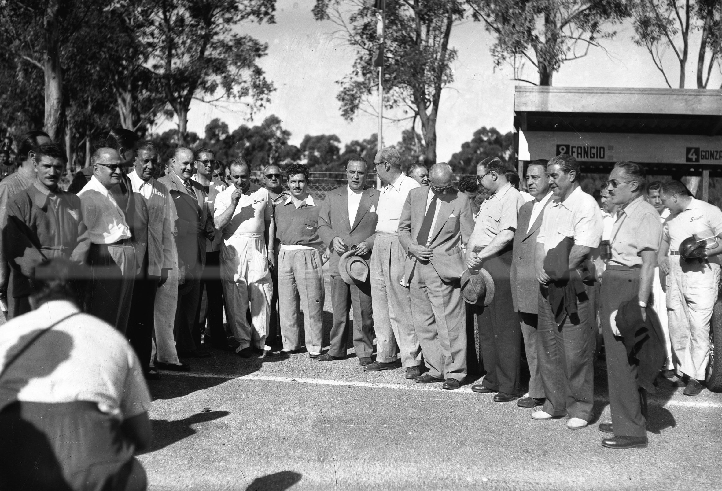 Pilotos y organizadores antes de la carrera. Fangio está al centro, todo vestido de blanco. Foto: Archivo El País.