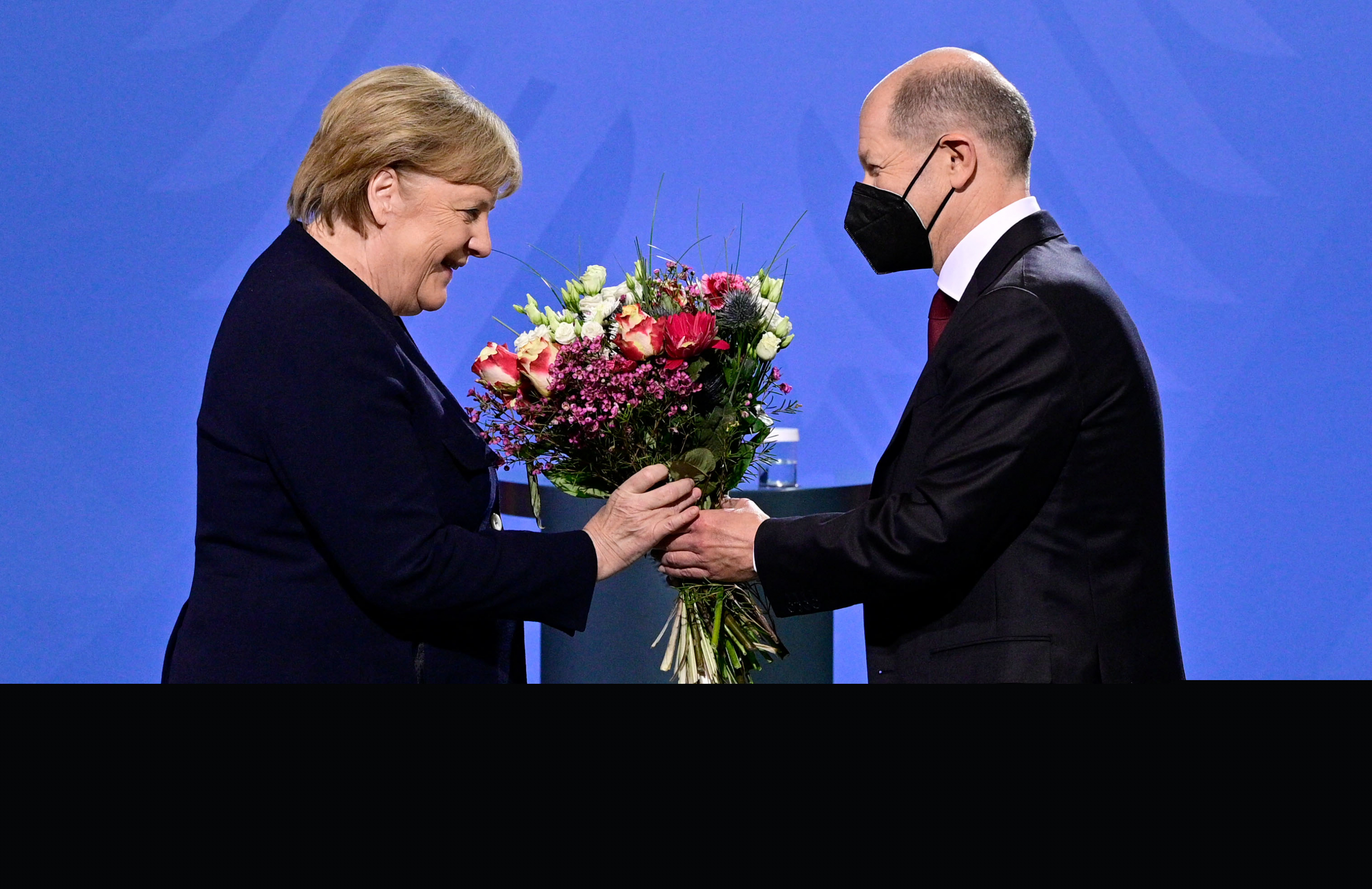 Olaf Scholz le entrega un ramo de flores a Angela Merkel. Foto: AFP