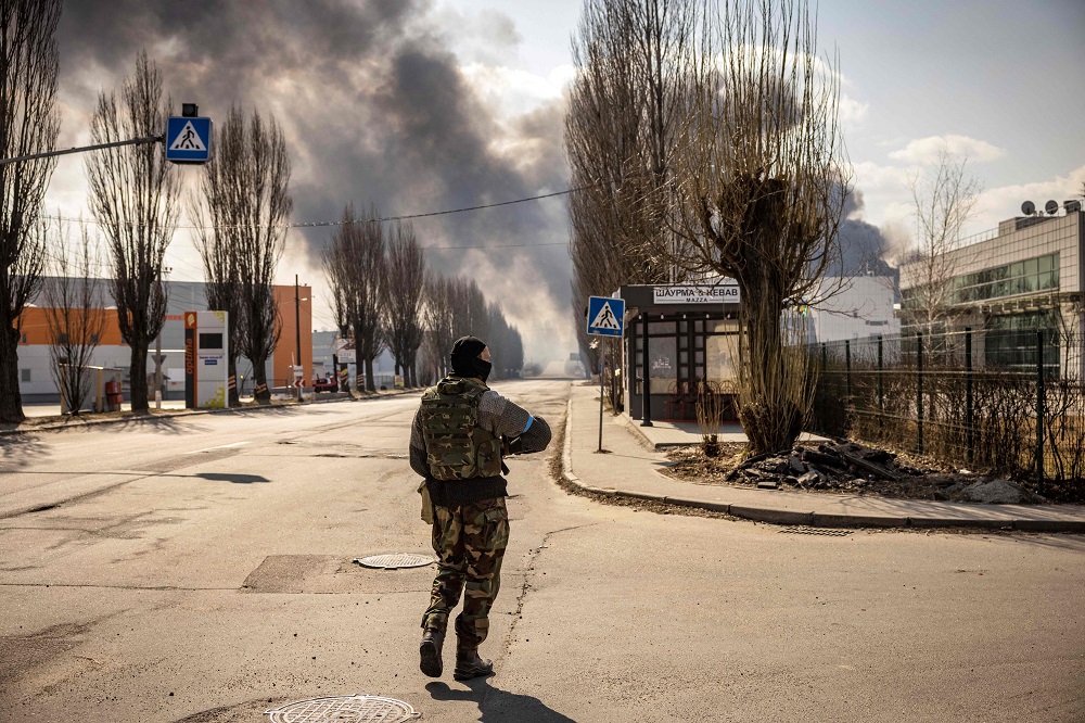 Un militar ucraniano hace guardia cerca de un almacén en llamas alcanzado por un proyectil ruso en los suburbios de Kiev. Foto: AFP.