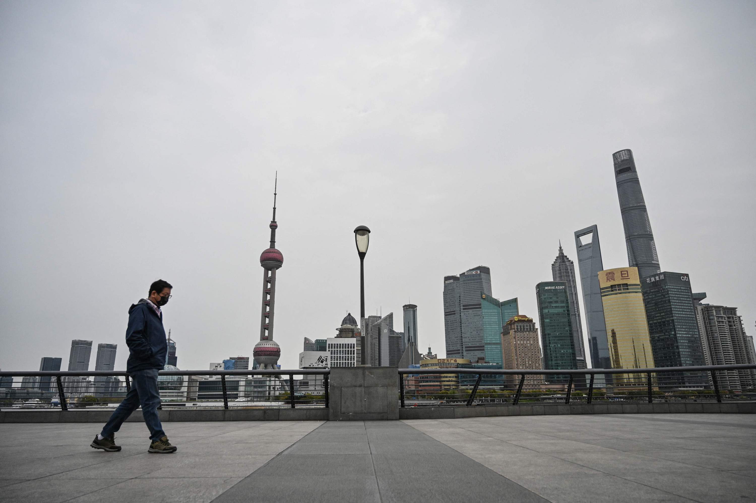 Hombre camina por el paseo marítimo del Bund a lo largo del río Huangpu mientras se ven edificios (atrás) en el distrito de Pudong, Shángai. Foto: AFP