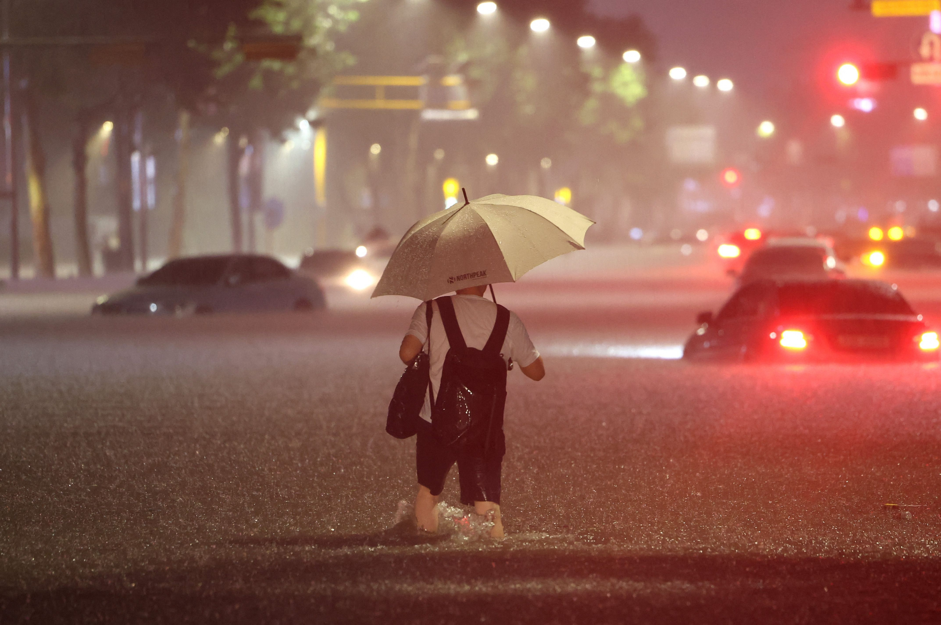 Un hombre camina junto a autos sumergidos en una calle durante fuertes lluvias en el distrito de Gangnam de Seúl. Foto: AFP